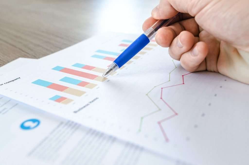 Hand holding a blue pen over printed charts for a project review.